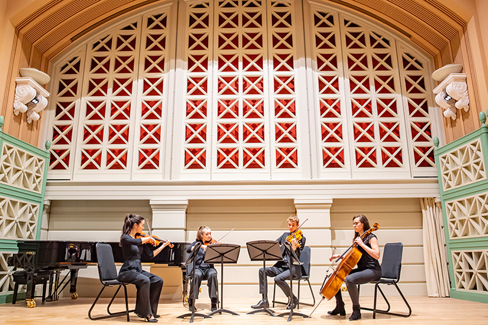 Students in a string quartet performing on stage in black attire.